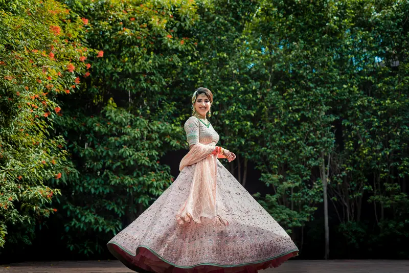 A bride twirling in a pale lehenga against green